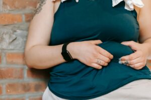 tattooed woman showing overweight belly near brick wall